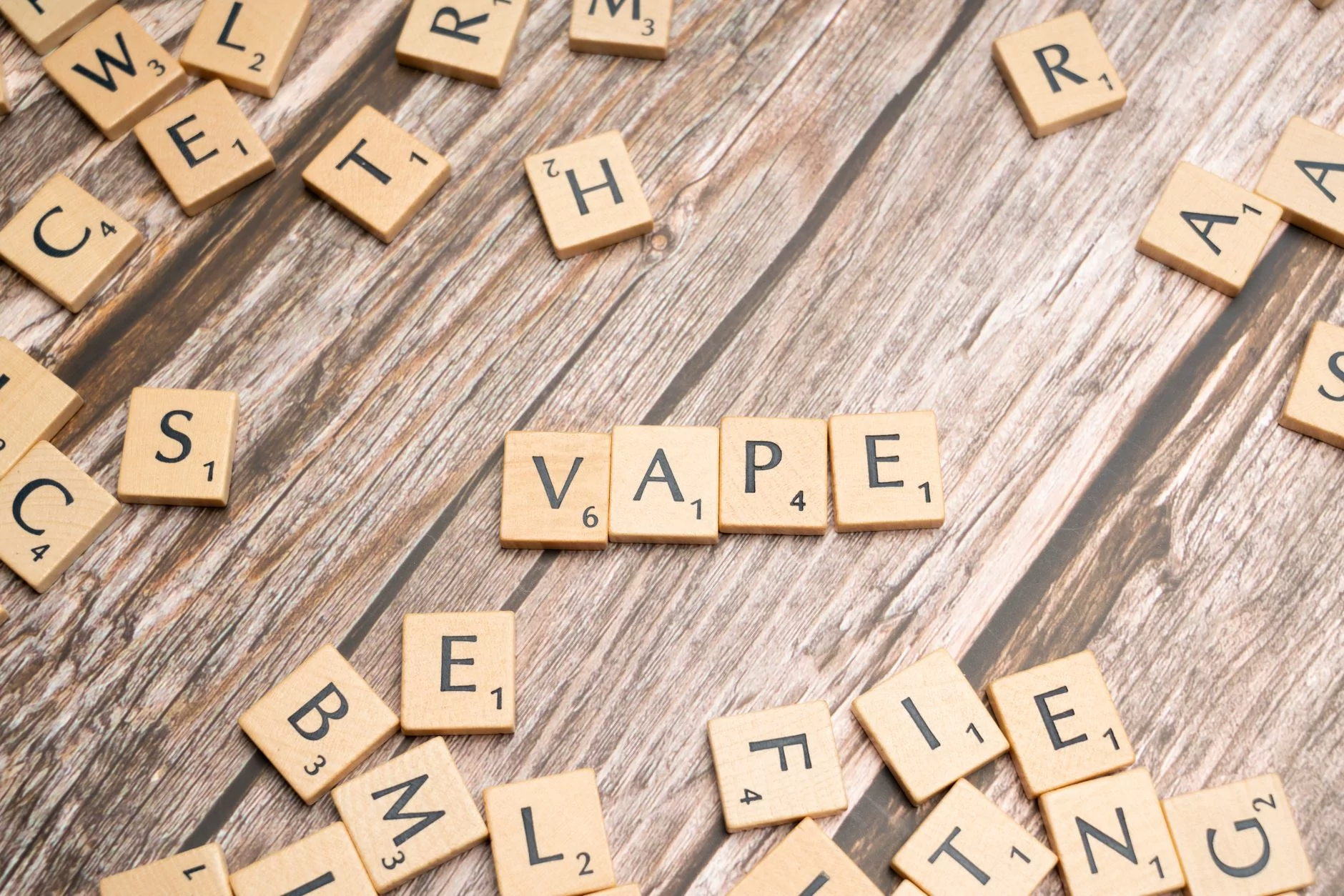 Wooden scrabble tiles with the word 'vape' on a textured wooden surface.